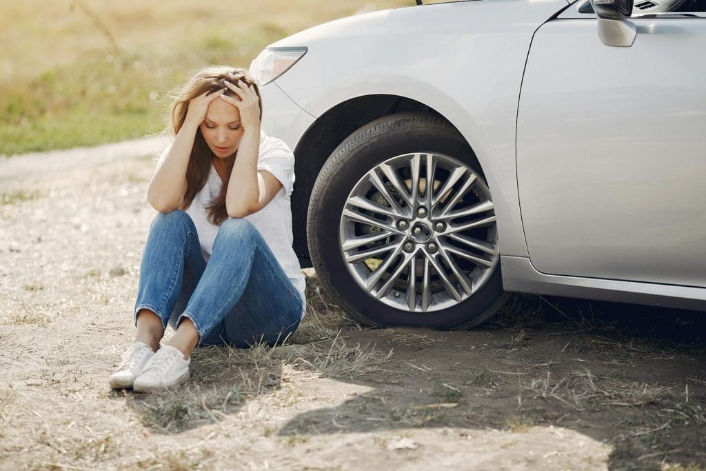 Modelo de petição de ação de reparação a título de danos morais e materiais por ter locado carro defeituoso em locadora de veículos 2 | Juristas Frustrated female driver in white t shirt and jeans sitting on ground near damaged car with hands on head during car travel in sunny summer day