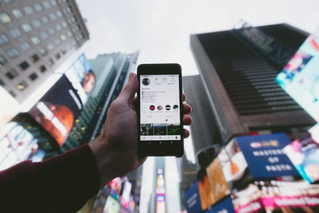 Modelo de petição de ação de reparação a título de danos morais e materiais por ser vítima de calúnia via Instagram 2 | Juristas high angle photo of person holding turned on smartphone with tall buildings background
