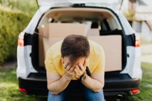 Modelo de petição de ação indenizatória em razão de inclusão indevida de nome de consumidor no Serasa Experian 1 | Juristas Faceless frustrated tired male wearing casual outfit sitting on car luggage boot and covering face with hands during relocation on sunny summer day